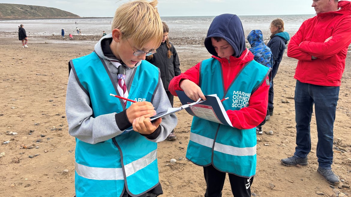 Two young people on a sandy beach write on litter survey forms