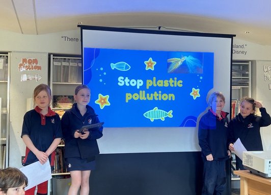 4 school children standing in front of a classroom. There is a presentation named "Stop Ocean Pollution" on the whiteboard