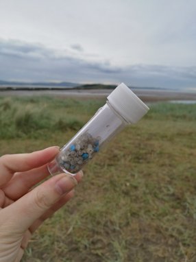 In a small test tube being held up by a hand, there are hundreds of tiny plastic pellets known as nurdles.