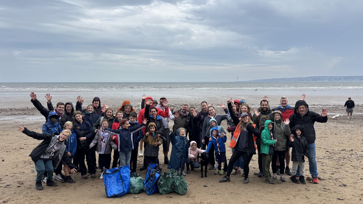 A large group shot of Copmanthorpe Scouts and their families smiling at the camera on Filey beach with the sea behind them