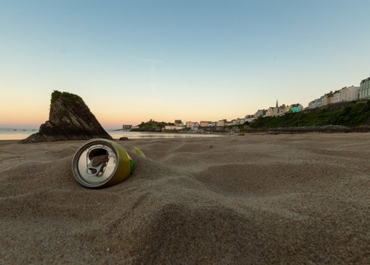 A close up of an aluminium can buried on a sandy beach