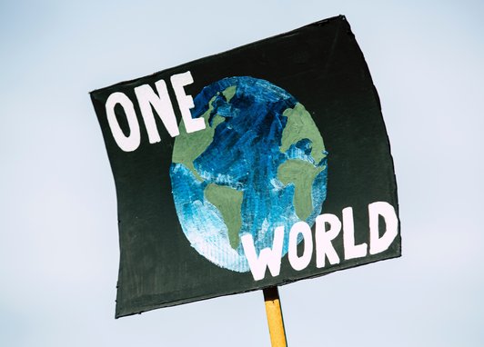 A cardboard campaign sigh that reads "One World" and an image of the Earth in the middle