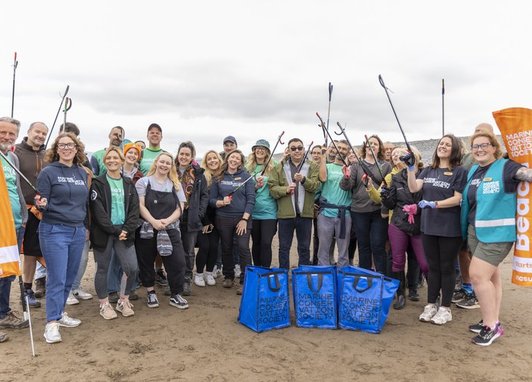 Great British Beach Clean 2025 holiday cottages group shot featuring around two dozen smiling people holding up litter grabs.