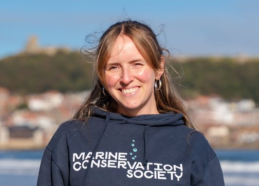 A landscape image of Marine Conservation Society staff member Lorna Donaghy, who is standing facing the camera wearing a dark blue Marine Conservation Society top