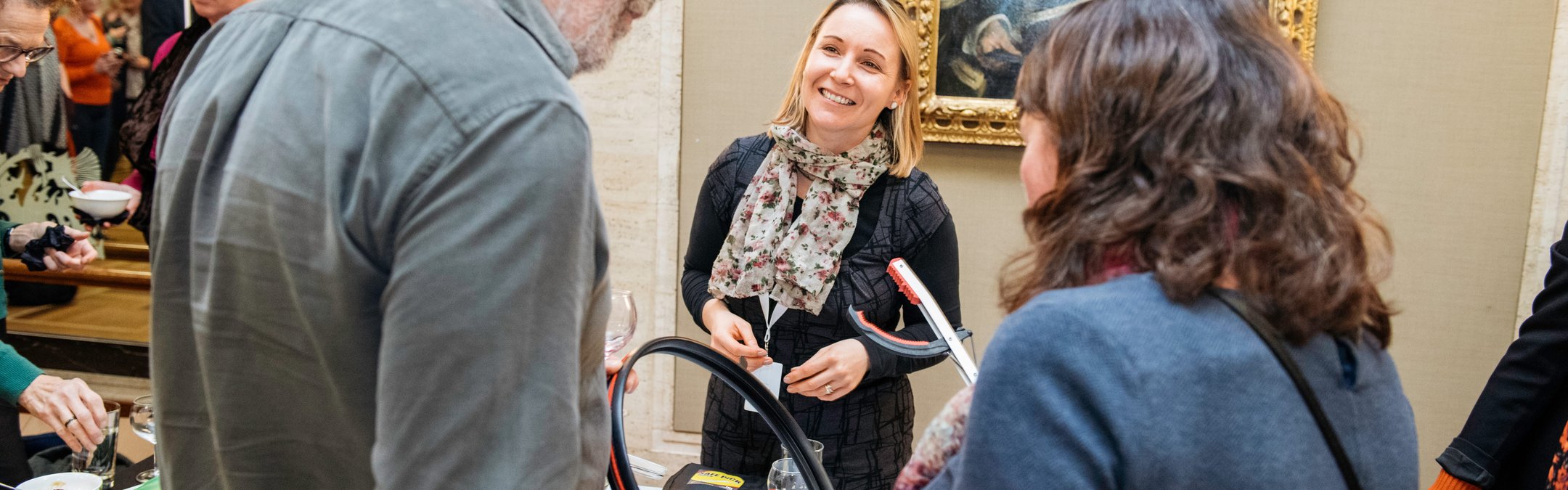 A man and a woman speaking with a smiling volunteer at a Marine Conservation Society display table. The man and women are holding litter picking items that were on the table.