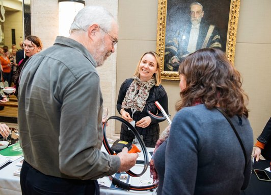 A man and a woman speaking with a smiling volunteer at a Marine Conservation Society display table. The man and women are holding litter picking items that were on the table.