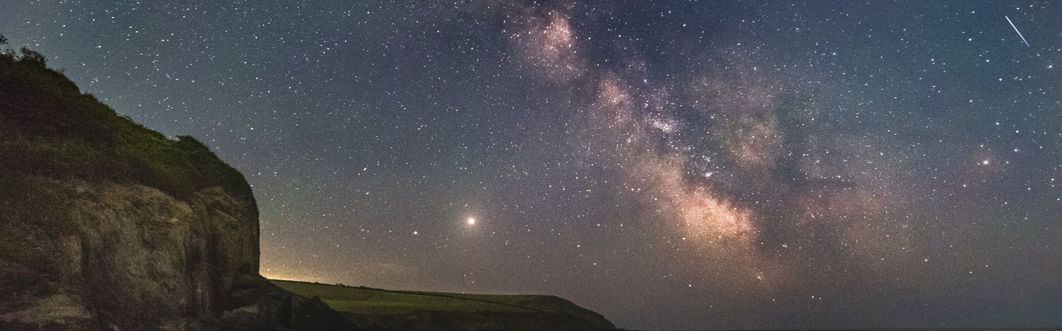 The night sky is shining with stars and the moon. Mothecombe coastline can be seen to the left of the photo, and the watery sand is reflecting the dark sky.