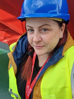 A picture of Bev wearing a hard hat and hi-vis jacket looking into the camera