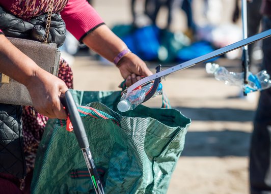 A close up of volunteers filling a bag with plastic bottles at a Scarborough beach clean.