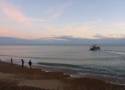 people on Hastings beach with a boat in the water