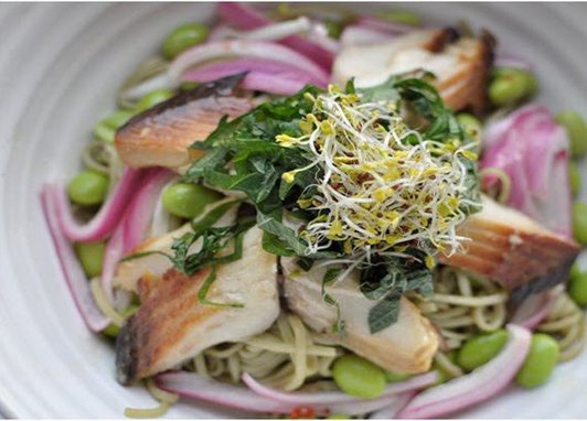 Arctic chard sits on a bed of noodles, with a salad and red onion garnish