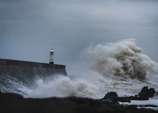 Large white waves hitting a wall at Porthcawl, Wales, with a dark grey sky above the coastline