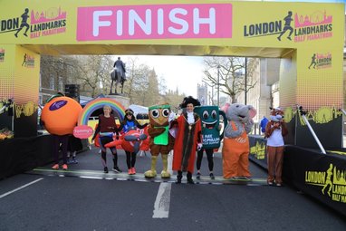 Runners in fancy dress costumes are stood underneath the finish line of the London Landmarks Half Marathon.