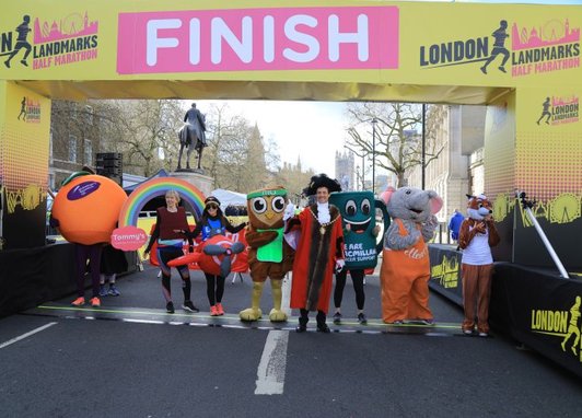 Runners in fancy dress costumes are stood underneath the finish line of the London Landmarks Half Marathon.