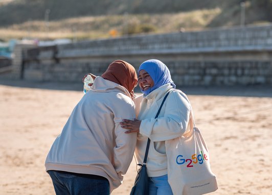 2 women laughing together on a beach.