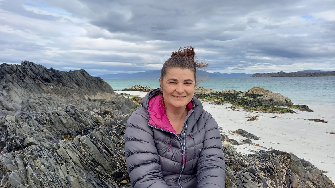 Anna Inman Restoration Forth's Shellfish Engagement Officer smiles from a beach while sat on a rock formation.
