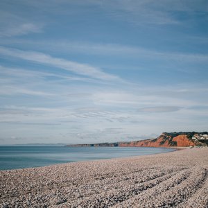 A coastal shot of Budleigh Salterton pebble beach. In the background, the distinctive red cliffs can be seen.