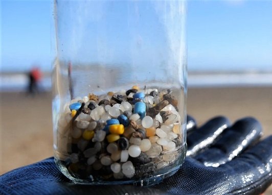 A gloved hand holds up a glass jar containing colourful plastic "nurdles", tiny pieces of plastic that were found during a beach clean