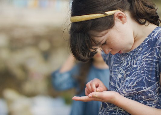 A girl studying a tiny shell she has in the palm of her hand