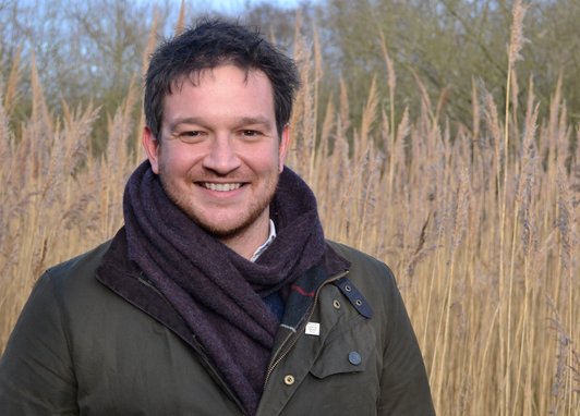 Professor Ben Garrod smiles at the camera with a reed bed backdrop.