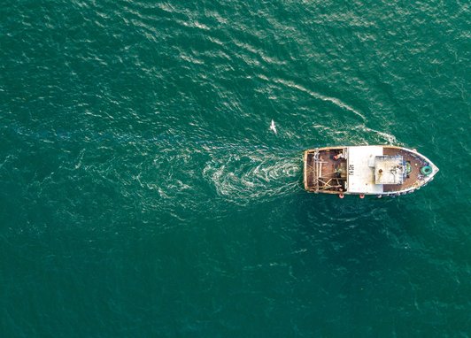 A small fishing trawler seen from a birds-eye-view over a deep blue ocean.