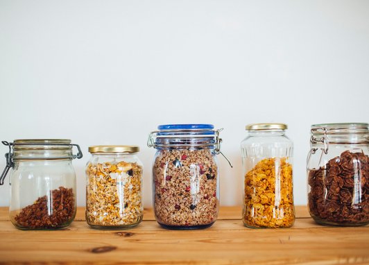 A row of glass jars on a shelf filled with different types of cereal