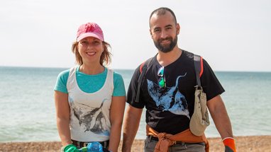 A man and a woman smiling at the camera on a shingle beach by the sea