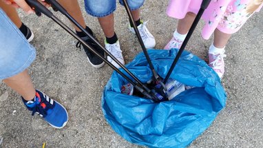 A group of children are using litterpickers to put rubbish into a blue refuse bag. Only the children's legs and feet can be seen.