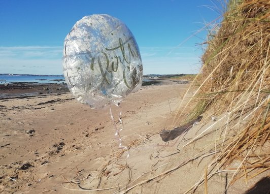 A deflated helium balloon is found on a sandy beach during a beach clean