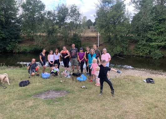 A group of volunteers posing for a photo on some grass while taking part in a Source to Sea clean. A river can be seen behind them.