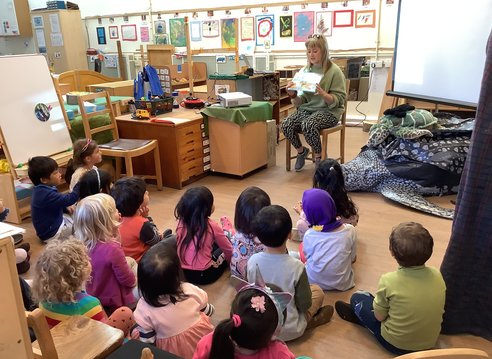 A member of Marine Conservation Society reading a book about a sea turtle to a group of young children sitting on the floor in a classroom.