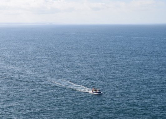An aerial shot of the ocean, with a small fishing boat to the right of the photograph.