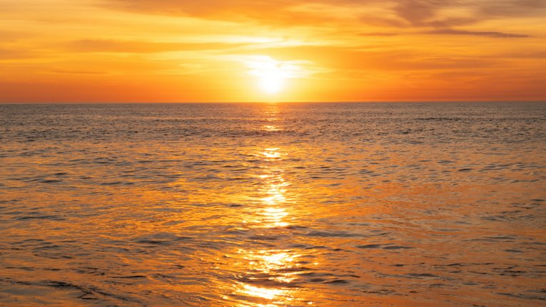 A shot of the open water during a sunset. The entire ocean surface is glowing orange