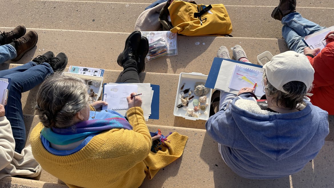 An image from above of a group of adults sitting on steps and creating artwork