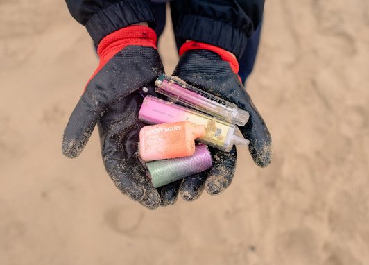A pair of gloved hands holding multiple-coloured vapes. The photo is from a top down view.
