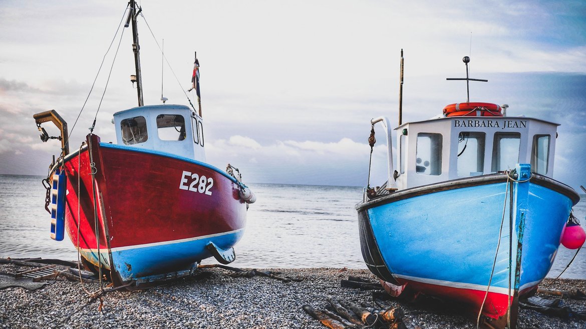 A close up of two fishing boats resting on pebbles. One boat is a vivid red colour, and the other is a bright blue colour.