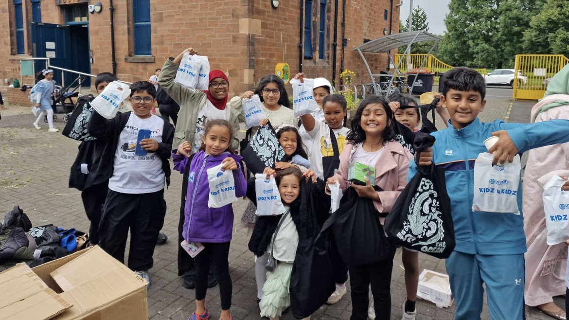 A group of young people in a school playground smile at the camera holding up nature-themed goodie bags