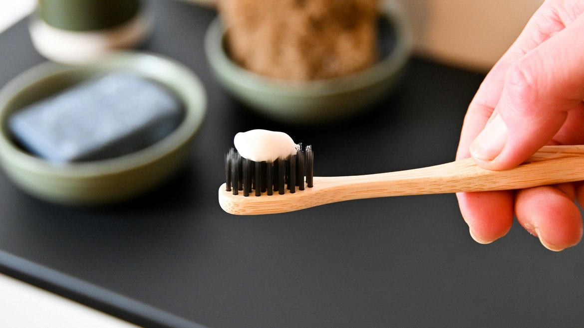 A hand holding a bamboo toothbrush with toothpaste on the end