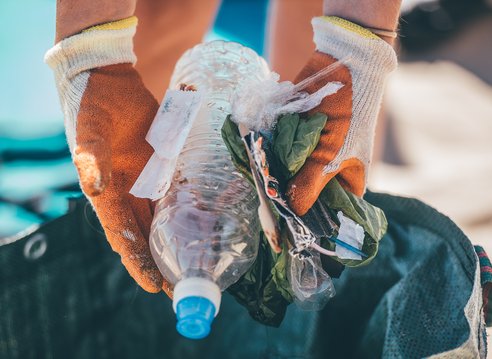 A pair of gloved hands holds a selection of plastic litter above a bag. The plastic litter was found during a beach clean