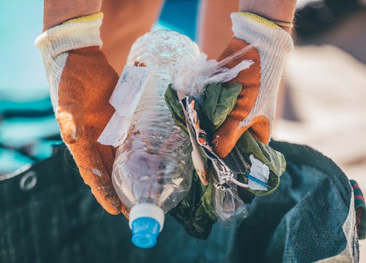 A pair of gloved hands holds a selection of plastic litter above a bag. The plastic litter was found during a beach clean