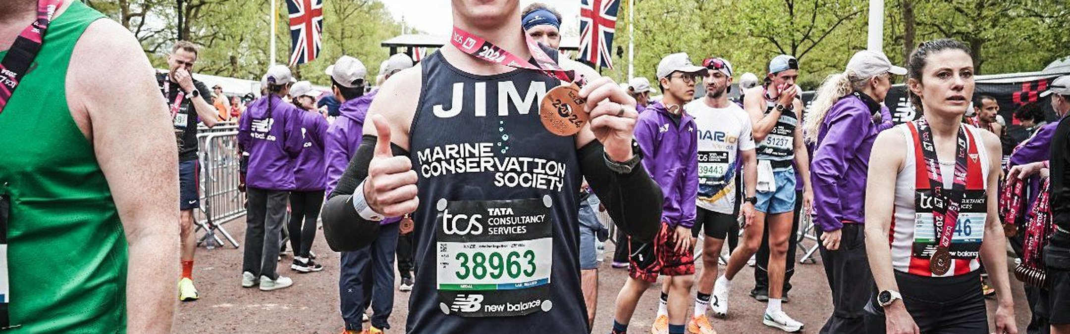 Jim Bourne stands at the end of the London Marathon, smiling at the camera as he holds up his well-earned finishers medal.