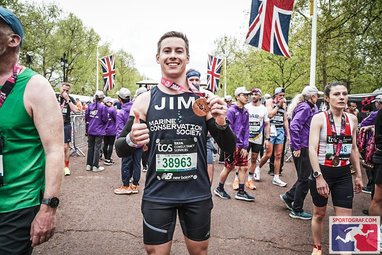 Jim Bourne stands at the end of the London Marathon, smiling at the camera as he holds up his well-earned finishers medal.