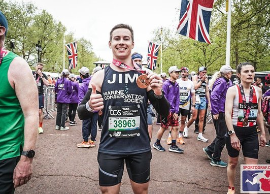 Jim Bourne stands at the end of the London Marathon, smiling at the camera as he holds up his well-earned finishers medal.