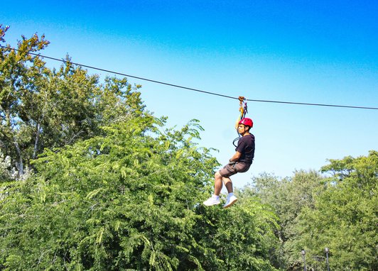 A man on a zipline, the trees can be seen below him