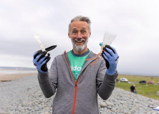 A man showing the camera pieces of debris found on the beach. He is holding a plastic fork, an oyster peg, some string, a popper and a plastic wrapper