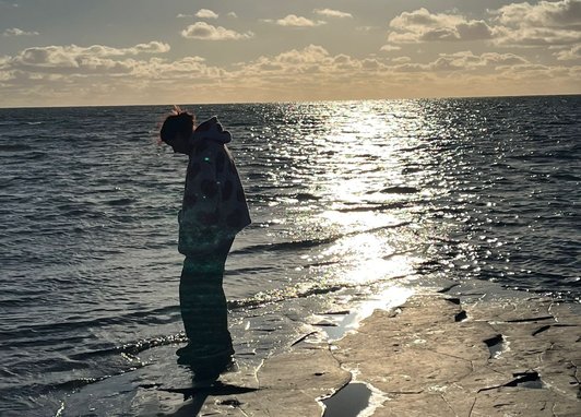 A silhouette of someone on a beach looking down. The tide is out and the sun is low.
