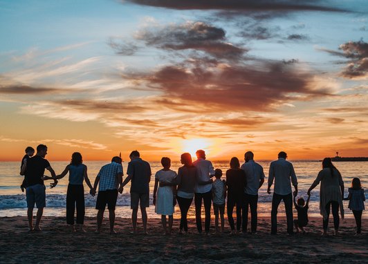 Multiple silhouettes of people on a beach. The setting sun is behind them causing the silhouettes