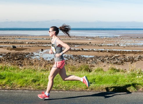 A runner on a paved path next to a rocky shoreline and the sea.